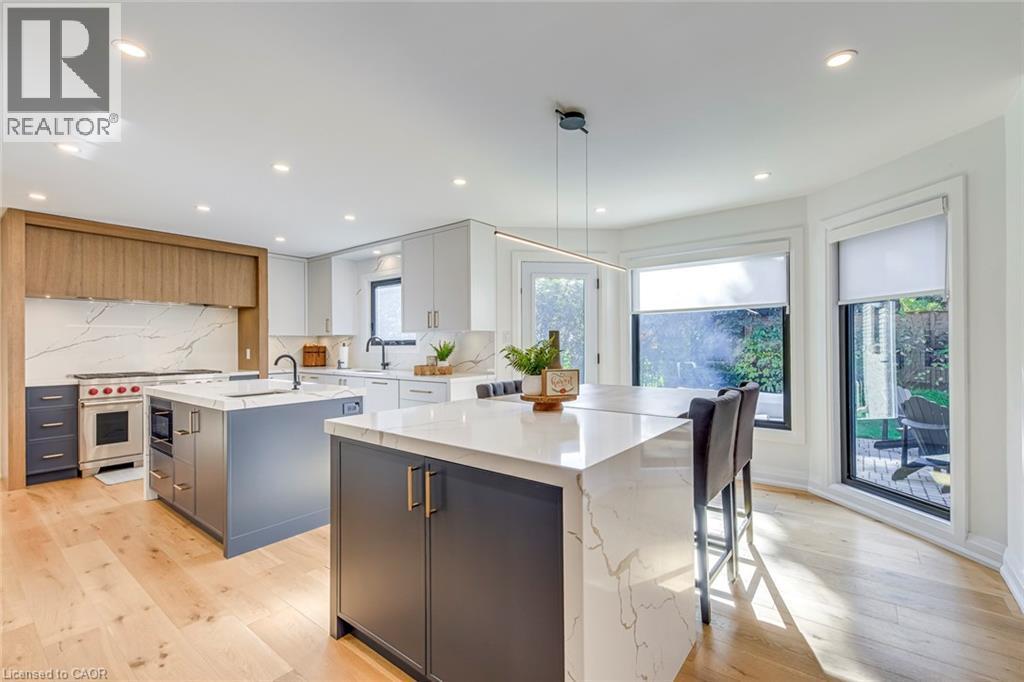 Gourmet kitchen featuring a dual-island layout with waterfall countertops, premium stainless steel appliances, light wood-finish flooring, and recessed lighting - 54 Deerview Avenue, Ancaster, ON - Indoor Photo Showing Kitchen With Upgraded Kitchen