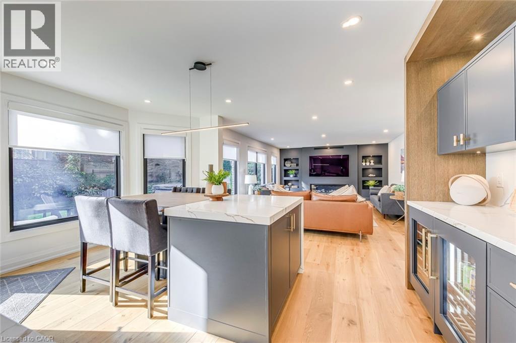 Modern kitchen island with a waterfall countertop, integrated bar seating, light wood-finish flooring, recessed lighting, and a built-in beverage cooler - 54 Deerview Avenue, Ancaster, ON - Indoor Photo Showing Kitchen With Upgraded Kitchen