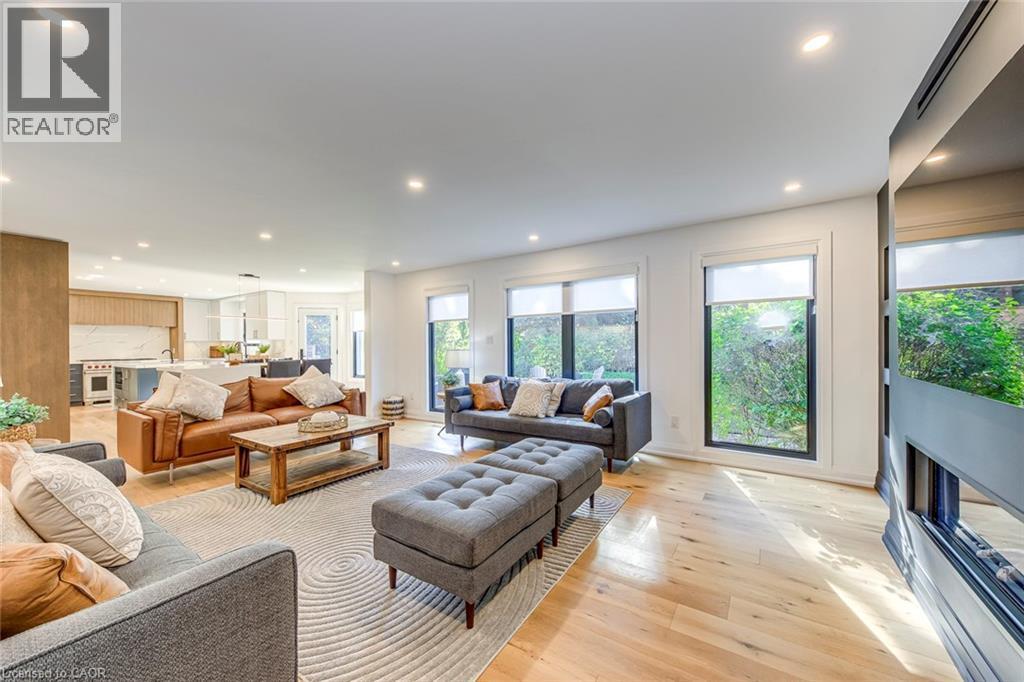 Open-concept living area featuring light wood-finish flooring, recessed lighting, and large windows with roller shades - 54 Deerview Avenue, Ancaster, ON - Indoor Photo Showing Living Room With Fireplace