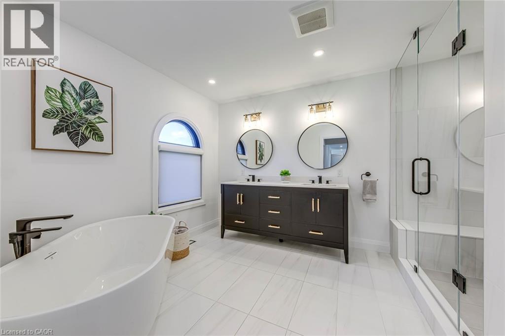 Freestanding soaking tub with dark bronze hardware, white tile flooring, and a glass-enclosed shower with integrated bench seating - 54 Deerview Avenue, Ancaster, ON - Indoor Photo Showing Bathroom