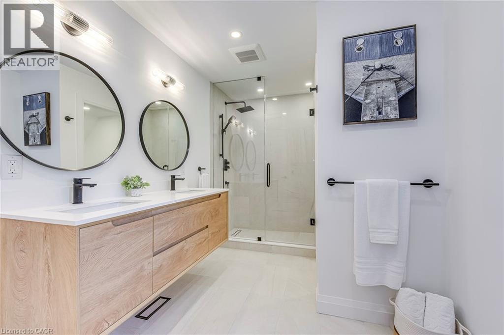 Modern bathroom featuring a floating wood-finish double vanity with integrated sinks and matte black faucets, paired with circular wall-mounted mirrors - 54 Deerview Avenue, Ancaster, ON - Indoor Photo Showing Bathroom