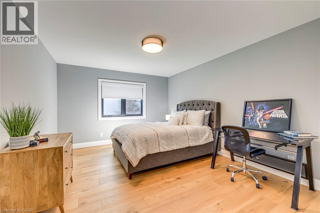 Room featuring light wood-finish flooring, a contemporary flush-mount ceiling light, and a window with a roller shade - 54 Deerview Avenue, Ancaster, ON - Indoor Photo Showing Bedroom