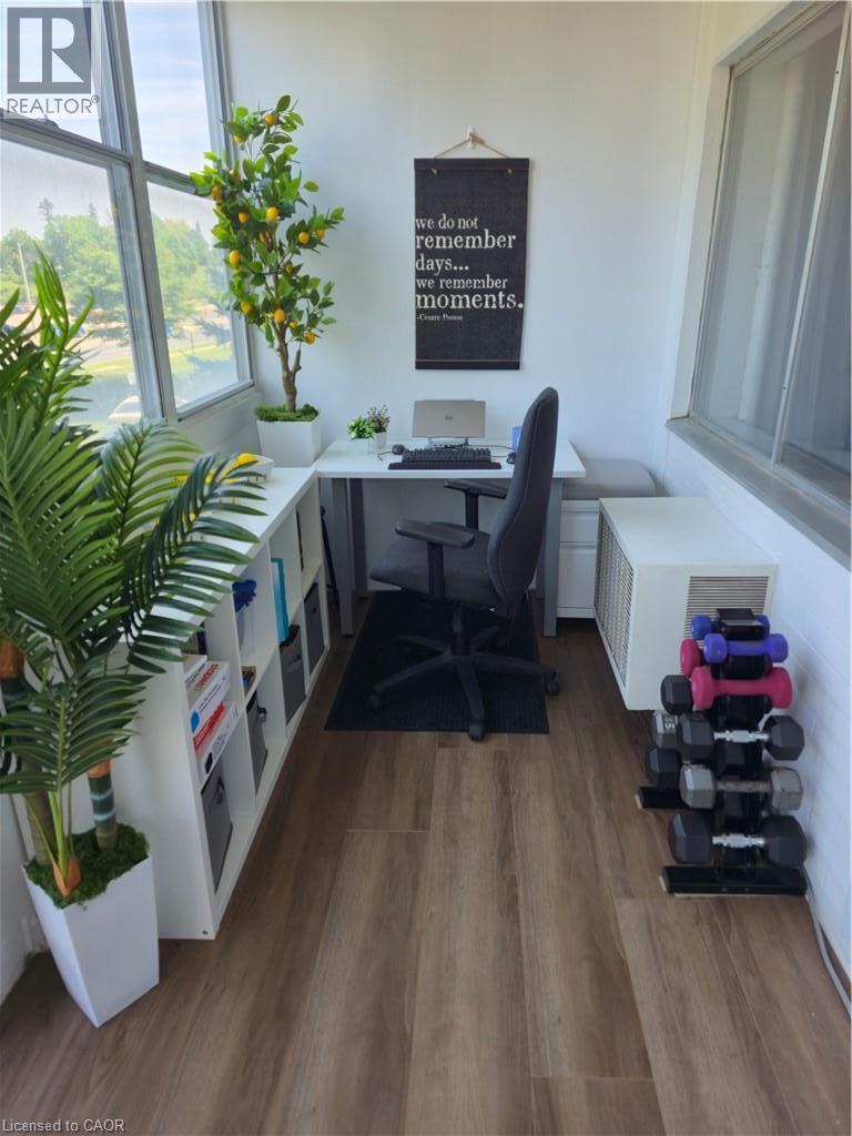 Enclosed balcony featuring wood-finish flooring, white built-in shelving, and expansive window panels - 45 Westmount Road N Unit# 202, Waterloo, ON - Indoor Photo Showing Office