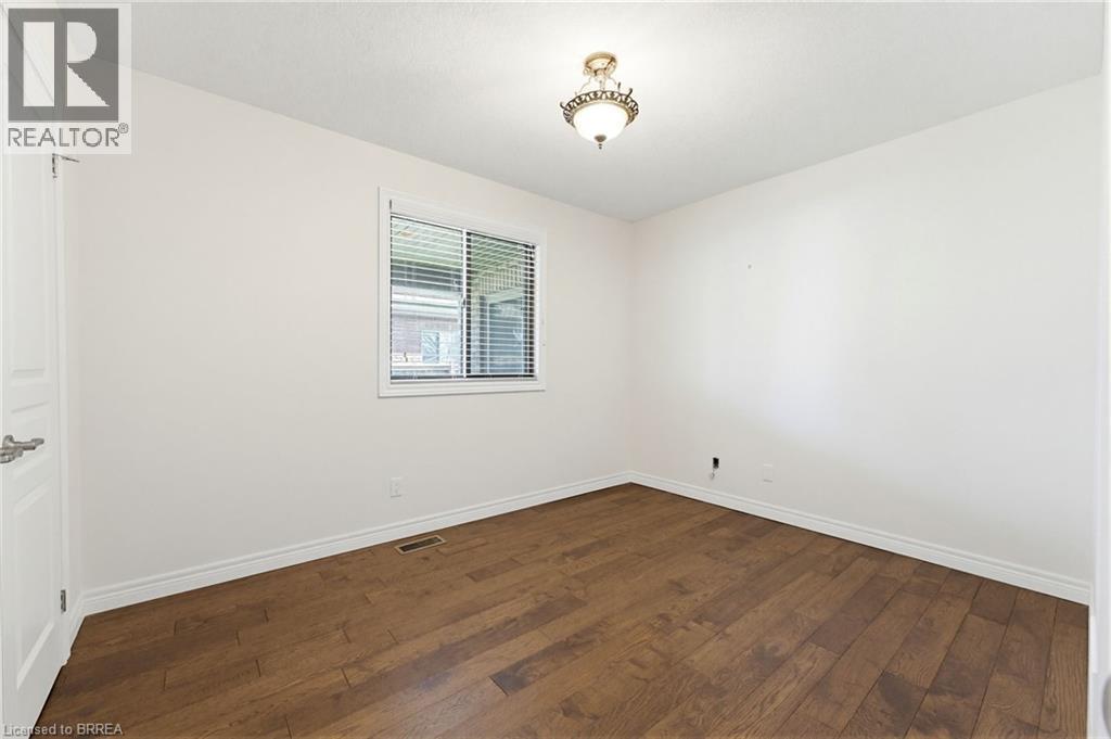 Bright interior room featuring a window with horizontal blinds, wood-finish flooring, white baseboards, and a classic-style ceiling light fixture - 6 General Street, Brantford, ON - Indoor Photo Showing Other Room