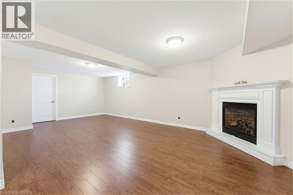 Spacious finished room featuring wood-finish flooring, a white trim baseboard, and a corner-set fireplace with a white mantle - 6 General Street, Brantford, ON - Indoor With Fireplace