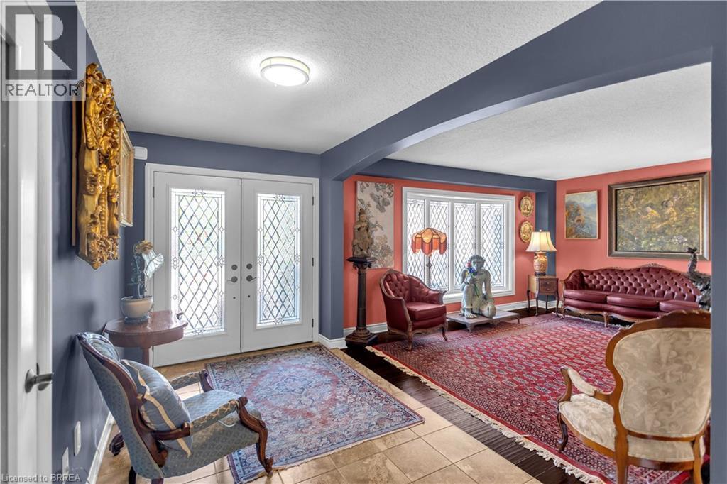 Entryway with double doors featuring decorative glass panels and a transom window, opening to a formal living space with a large picture window - 69 Hunter Way, Brantford, ON - Indoor