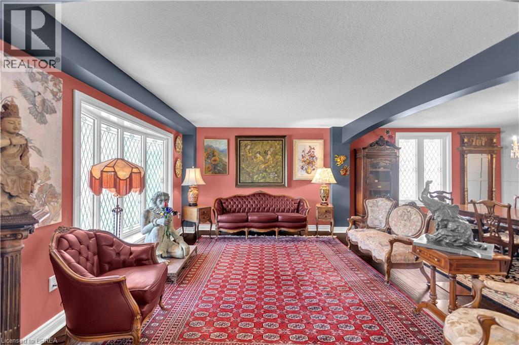 Spacious interior room featuring decorative picture windows, a detailed chandelier, and wood-finish flooring partially covered by a large area rug - 69 Hunter Way, Brantford, ON - Indoor Photo Showing Living Room