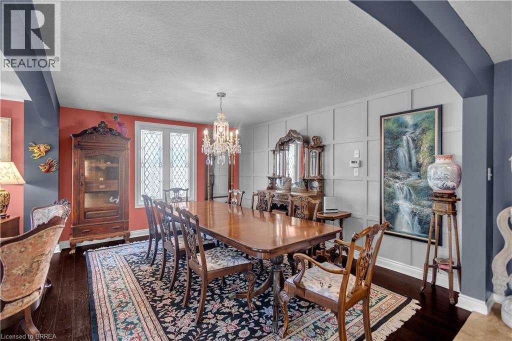 Formal dining space featuring dark wood-finish flooring, a crystal chandelier, decorative wall paneling, and a window with diamond-patterned mullions - 69 Hunter Way, Brantford, ON - Indoor Photo Showing Dining Room