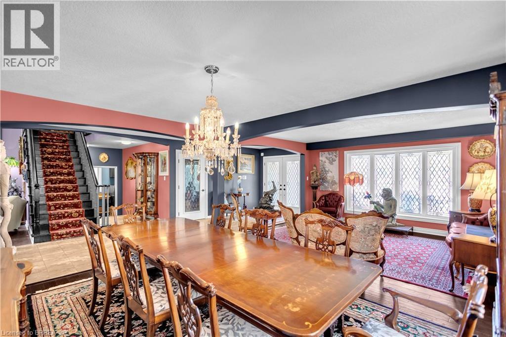 Formal dining area featuring a crystal chandelier, patterned area rugs, a large multi-pane window with diamond grilles, and a staircase with a patterned runner - 69 Hunter Way, Brantford, ON - Indoor Photo Showing Dining Room