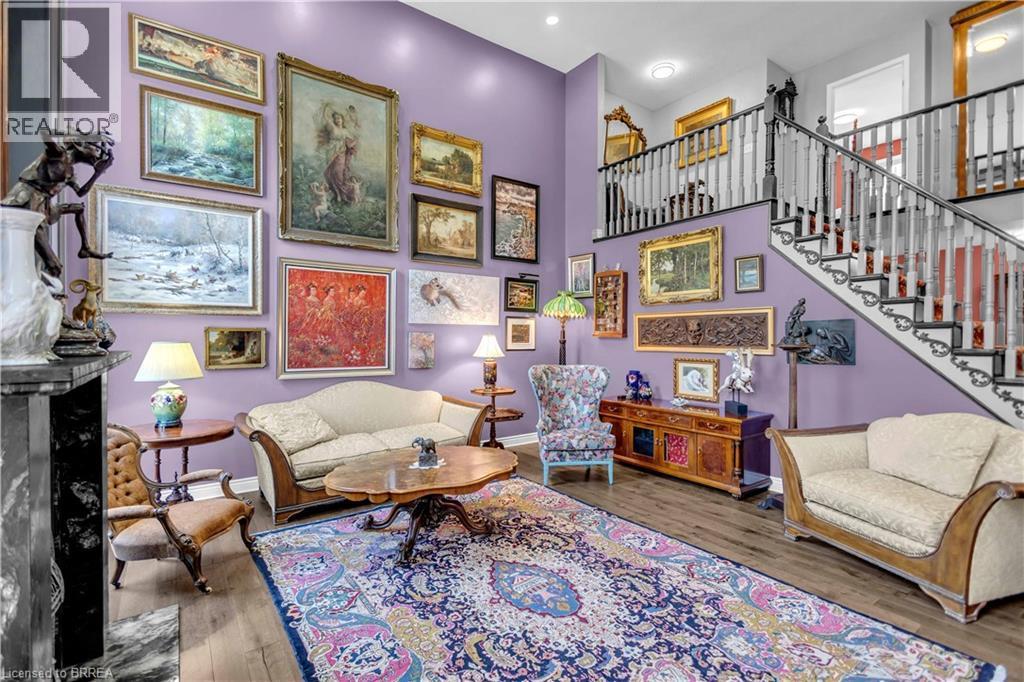 Two-story living area featuring wood-finish flooring, a grand staircase with white balusters and dark handrails, and a prominent fireplace with a dark marble surround - 69 Hunter Way, Brantford, ON - Indoor