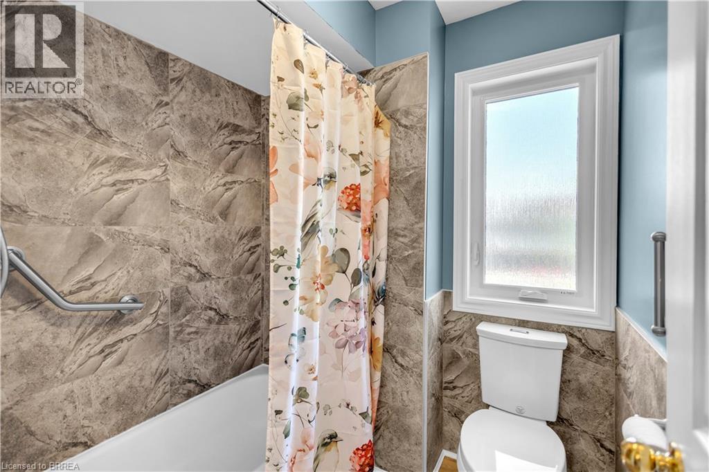 Bathroom featuring a white bathtub with a grab bar, large format stone-look wall tiles, and a white framed window with privacy glass - 69 Hunter Way, Brantford, ON - Indoor Photo Showing Bathroom