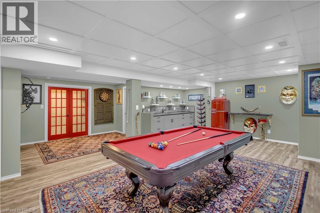 Recreation space featuring wood-finish flooring, a drop ceiling with recessed lighting, red French doors, and a built-in wet bar with cabinetry - 69 Hunter Way, Brantford, ON - Indoor Photo Showing Other Room