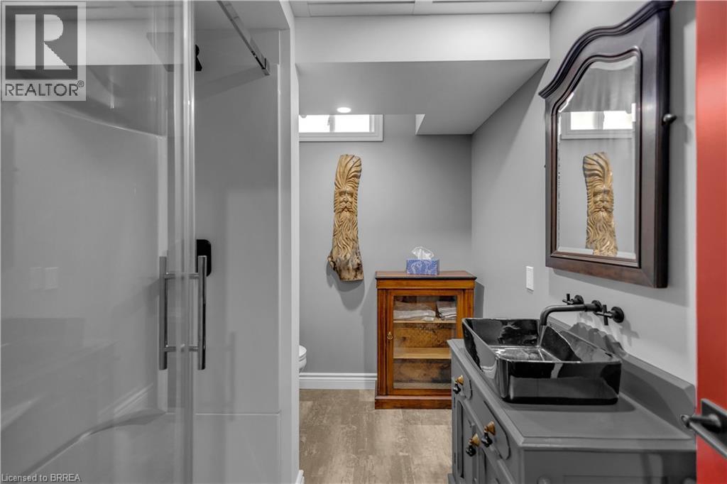 Bathroom featuring a glass-enclosed shower, a vanity with a black vessel sink and wall-mounted faucet, and wood-finish flooring - 69 Hunter Way, Brantford, ON - Indoor