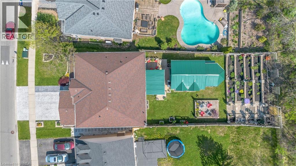 Expansive backyard featuring a green metal-roofed structure, raised garden beds, a concrete patio, and a fire pit area - 69 Hunter Way, Brantford, ON - Outdoor With View