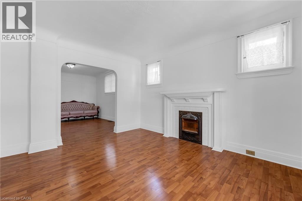 Spacious interior room featuring wood-finish flooring, a traditional white mantel with a dark fireplace surround, and multiple windows - 168 Britannia Avenue, Hamilton, ON - Indoor With Fireplace