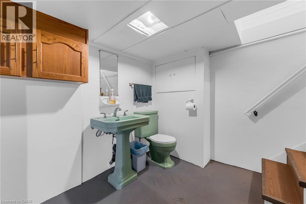 Bathroom featuring a pedestal sink, toilet, wall-mounted mirror, and built-in wood cabinetry - 168 Britannia Avenue, Hamilton, ON - Indoor