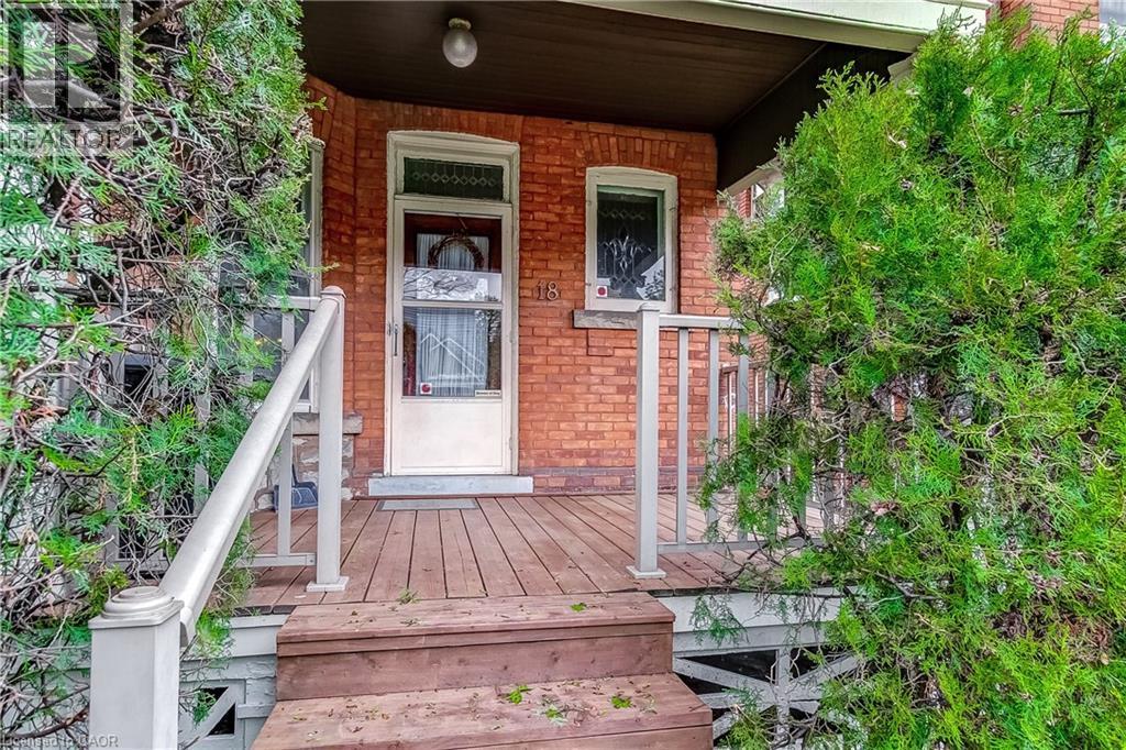 Brick facade home featuring a wood deck entry with white railings, wood steps, and mature evergreen shrubs - 18 Fairleigh Crescent, Hamilton, ON - Outdoor