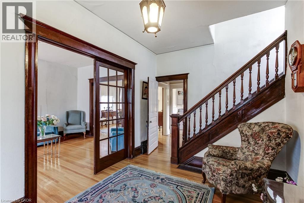 Grand entry hall with a dark wood staircase featuring turned balusters, light wood-finish flooring, and a glass-paneled pocket door - 18 Fairleigh Crescent, Hamilton, ON - Indoor Photo Showing Other Room