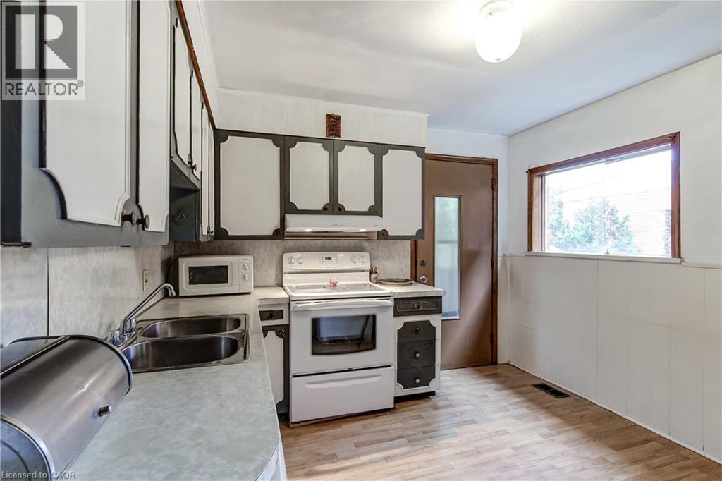 Kitchen featuring overhead and base cabinetry, double basin stainless steel sink, and white appliances - 18 Fairleigh Crescent, Hamilton, ON - Indoor Photo Showing Kitchen With Double Sink