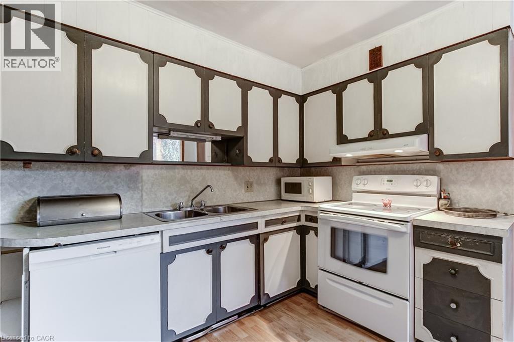 Corner kitchen with wood-finish flooring, white appliances, and a double basin sink - 18 Fairleigh Crescent, Hamilton, ON - Indoor Photo Showing Kitchen With Double Sink
