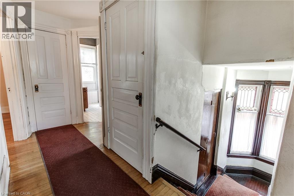 Hardwood flooring throughout the hallway and staircase, featuring white paneled doors with dark hardware, a dark wood handrail, and a bay window with decorative glass panels - 18 Fairleigh Crescent, Hamilton, ON - Indoor Photo Showing Other Room