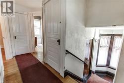 Hardwood flooring throughout the hallway and staircase, featuring white paneled doors with dark hardware, a dark wood handrail, and a bay window with decorative glass panels -