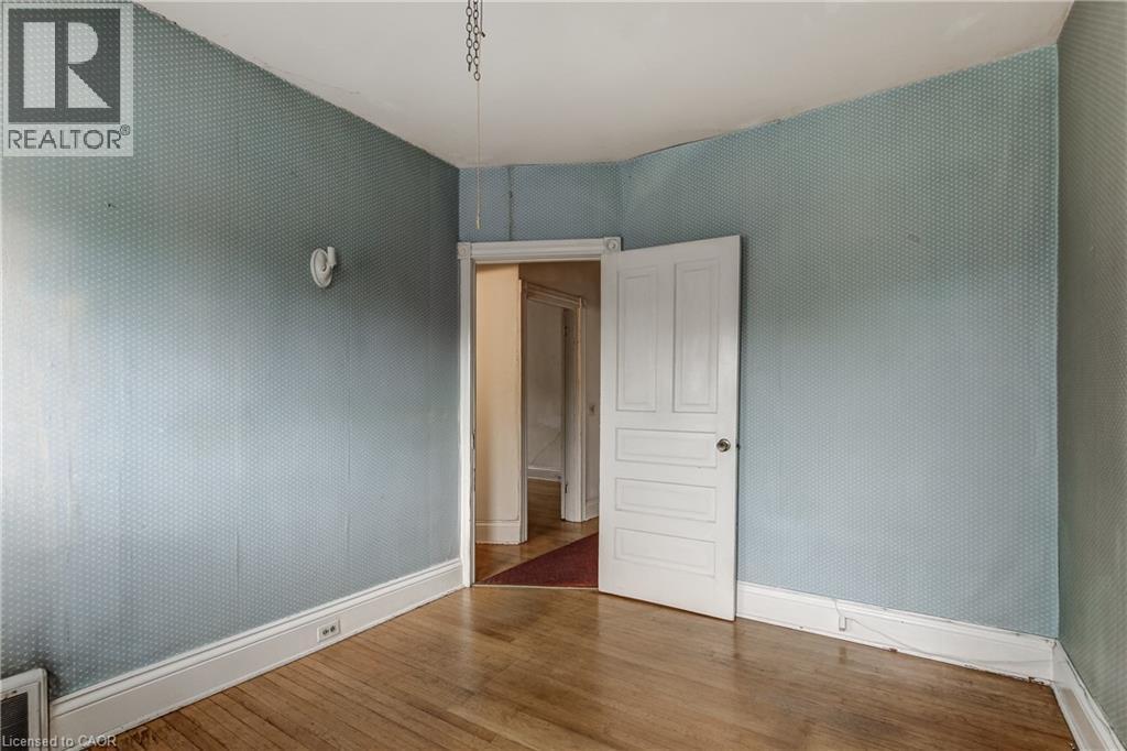 Room featuring wood-finish flooring, patterned wallpaper, white baseboards, and a paneled interior door - 18 Fairleigh Crescent, Hamilton, ON - Indoor Photo Showing Other Room