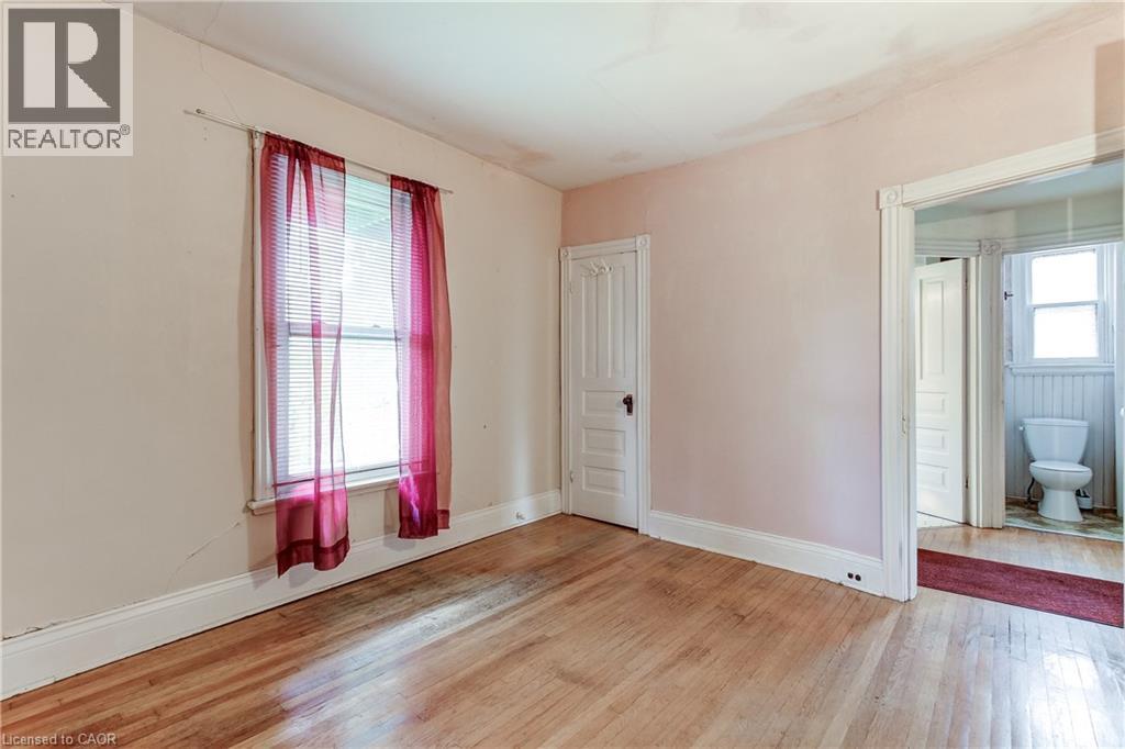 Hardwood flooring throughout, featuring a window with blinds, a paneled door, and white baseboards - 18 Fairleigh Crescent, Hamilton, ON - Indoor Photo Showing Other Room