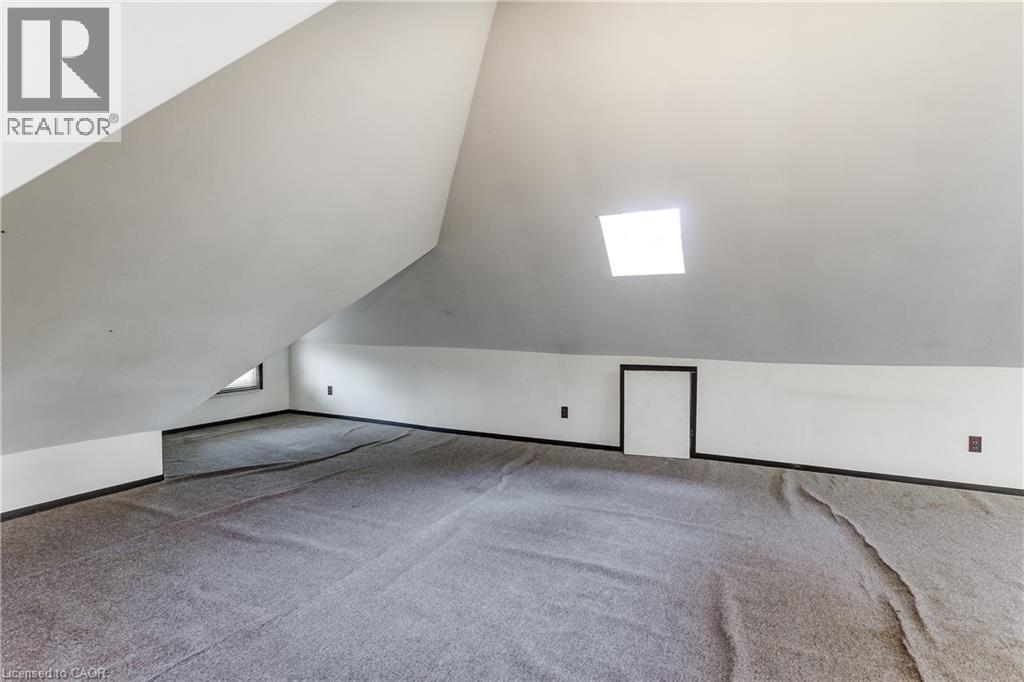 Sloped ceiling interior space featuring a skylight, gray carpeting, a built-in access panel, and a small window - 18 Fairleigh Crescent, Hamilton, ON - Indoor Photo Showing Other Room