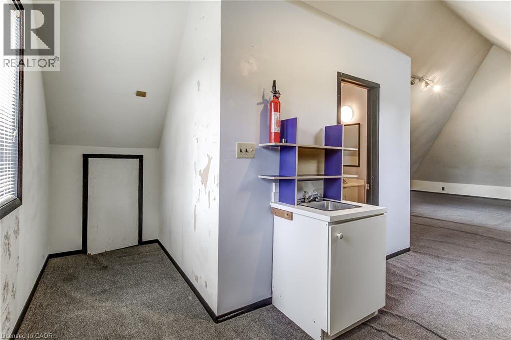 Compact kitchenette with a stainless steel sink, built-in shelving, and white base cabinetry, complemented by sloped ceilings and gray carpeting - 18 Fairleigh Crescent, Hamilton, ON - Indoor Photo Showing Other Room