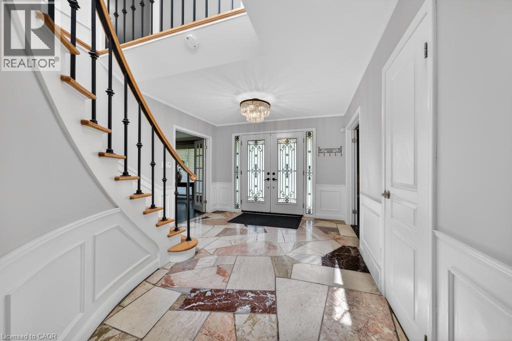 Entry foyer featuring irregular flagstone-style flooring, a curved staircase with wood treads and black iron balusters, white wainscoting, and a crystal flush-mount light fixture - 25 Braemar Place, Hamilton, ON - Indoor Photo Showing Other Room