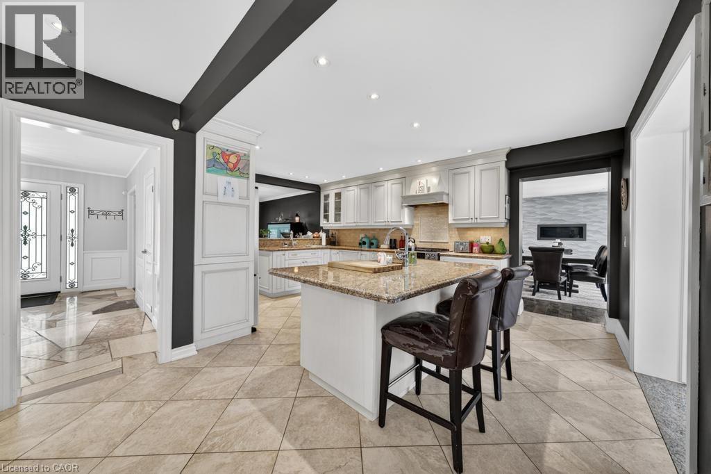 Spacious kitchen featuring an island with stone countertop, white cabinetry, integrated stainless steel appliances, recessed lighting, and tile flooring - 25 Braemar Place, Hamilton, ON - Indoor