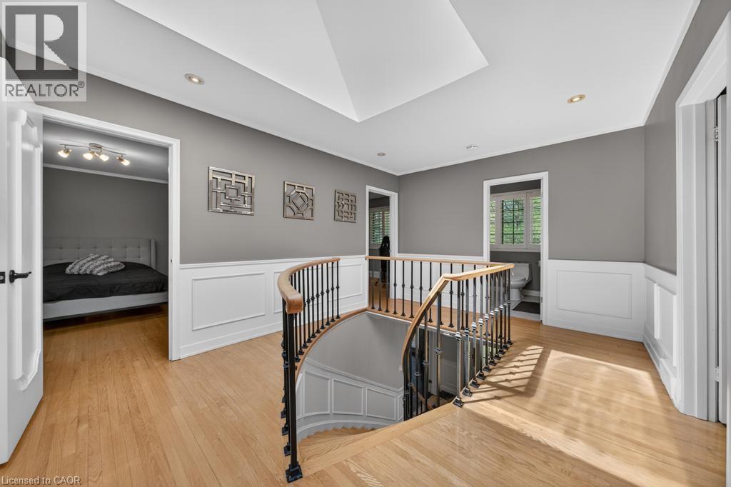 Hardwood flooring extends throughout this upper-level landing, featuring a graceful curved staircase with a dark iron and wood-finish railing - 25 Braemar Place, Hamilton, ON - Indoor