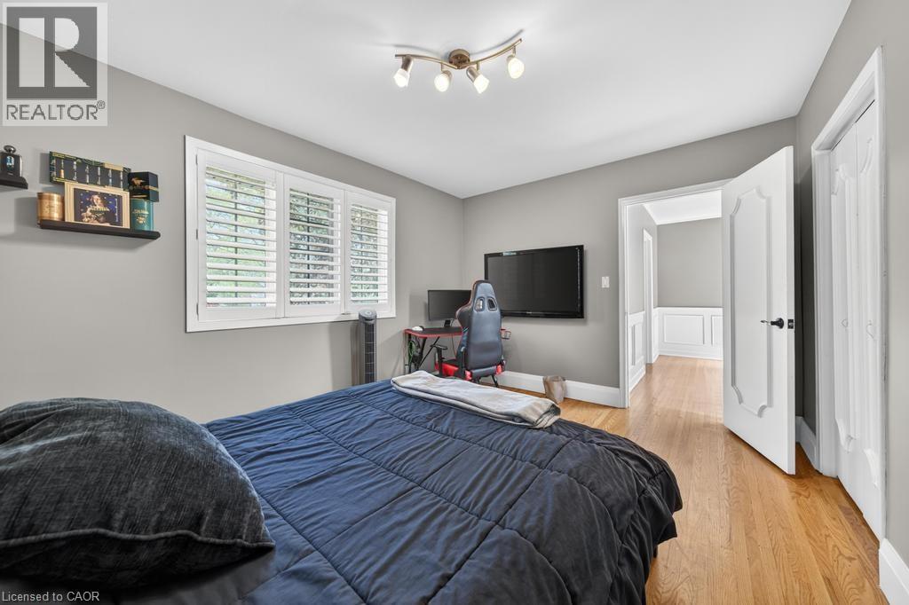 Bedroom featuring hardwood flooring, white plantation shutters, a multi-bulb track light fixture, grey wall paint, and a paneled doorway - 25 Braemar Place, Hamilton, ON - Indoor Photo Showing Bedroom