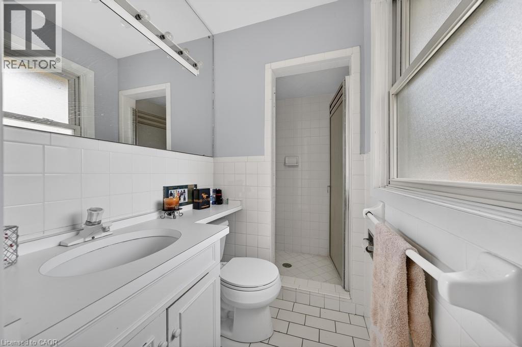 Bathroom featuring a single vanity with integrated sink, white tile flooring, white wall tiling, a frosted window, and a shower with a sliding glass door - 25 Braemar Place, Hamilton, ON - Indoor Photo Showing Bathroom