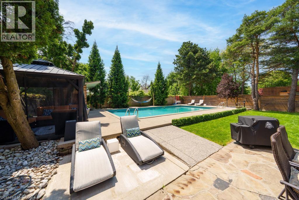 Private backyard oasis featuring a rectangular swimming pool with surrounding concrete decking, a screened gazebo, a flagstone patio, and mature landscaping - 25 Braemar Place, Hamilton, ON - Outdoor With In Ground Pool With Backyard
