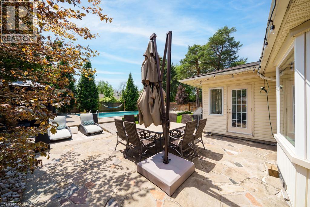 Expansive stone patio featuring a rectangular dining area, an in-ground pool, and a dedicated lounge space - 25 Braemar Place, Hamilton, ON - Outdoor