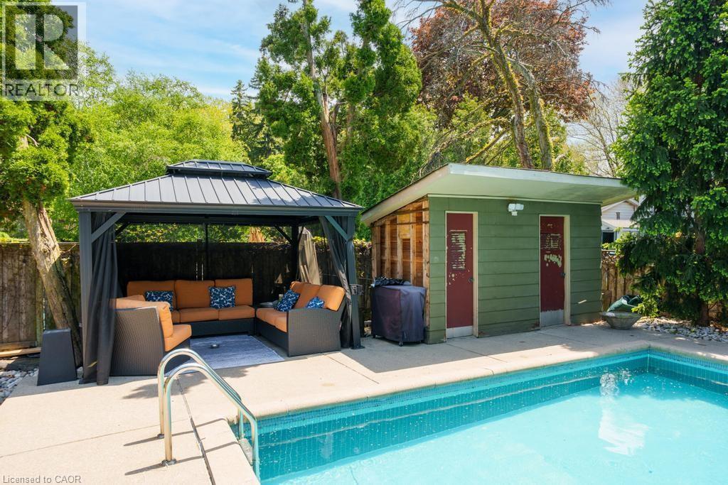 Outdoor pool area featuring a built-in pool, a dedicated pool house with two entry doors, a structured gazebo, and mature perimeter trees - 25 Braemar Place, Hamilton, ON - Outdoor With In Ground Pool With Deck Patio Veranda