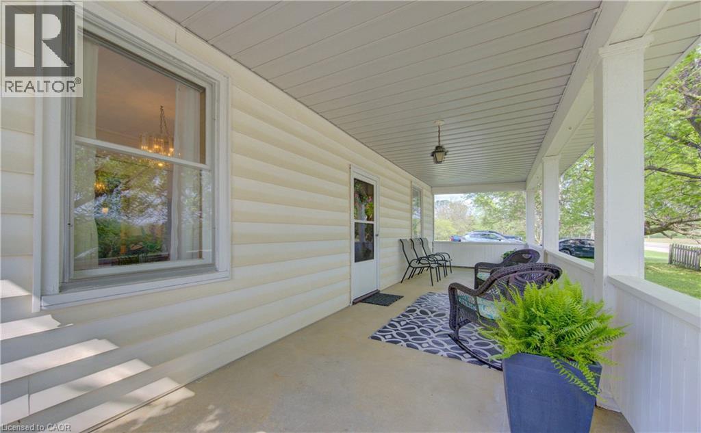 Expansive covered porch featuring a concrete floor, white vinyl siding, white support pillars, and a ceiling-mounted light fixture - 1463 Kossuth Road, Cambridge, ON - Outdoor With Deck Patio Veranda With Exterior