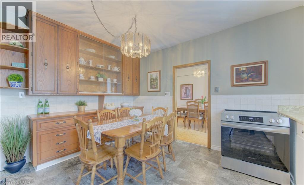 Eat-in kitchen featuring wood cabinetry with glass-front uppers, a built-in stainless steel range, light-toned tiled backsplash, and stone-look flooring - 1463 Kossuth Road, Cambridge, ON - Indoor Photo Showing Dining Room