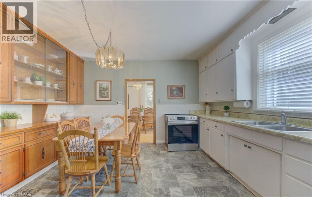 Kitchen dining area featuring a clear glass chandelier, light wood cabinetry with glass-front uppers, white shaker-style base cabinets, a stainless steel range, and a dual basin sink - 1463 Kossuth Road, Cambridge, ON - Indoor Photo Showing Kitchen With Double Sink