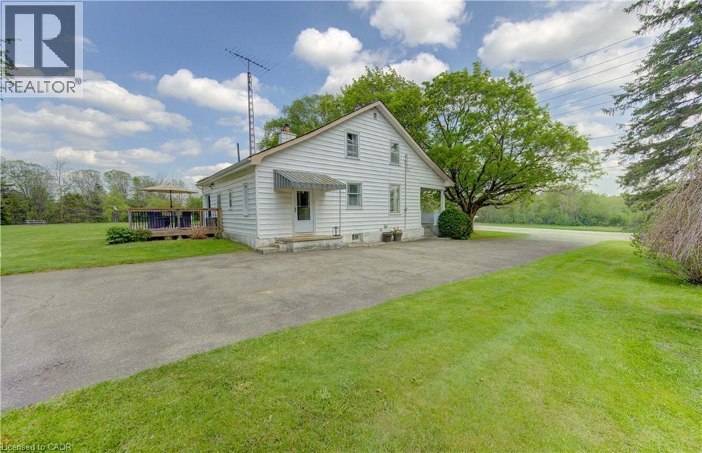 White sided residence featuring a front door awning, an expansive lawn, a paved driveway, and a rear wood deck - 1463 Kossuth Road, Cambridge, ON - Outdoor