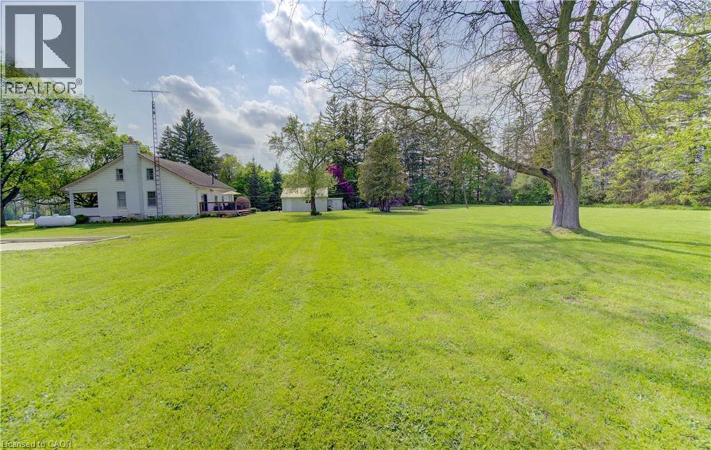 Expansive green lawn with mature trees and a distant white residential structure featuring a deck - 1463 Kossuth Road, Cambridge, ON - Outdoor