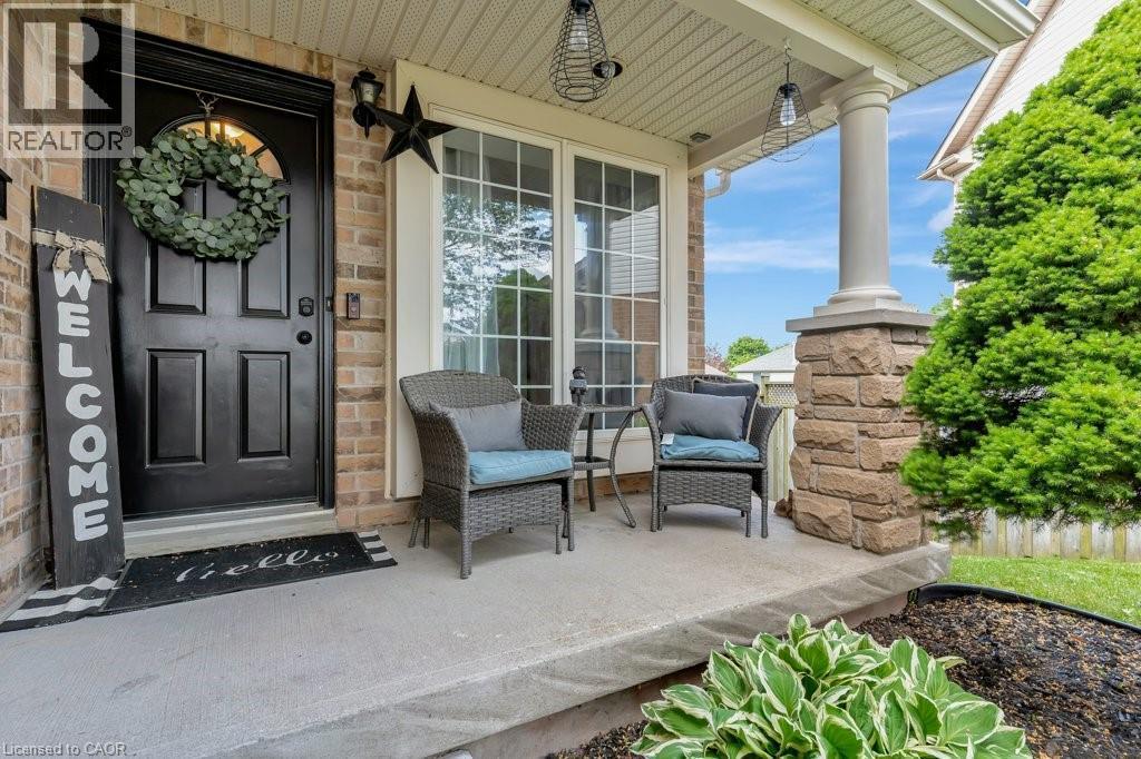 Brick facade with a covered porch featuring a decorative stone base column, a panel-style entry door, and large casement windows - 49 Small Court, Cambridge, ON - Outdoor With Deck Patio Veranda