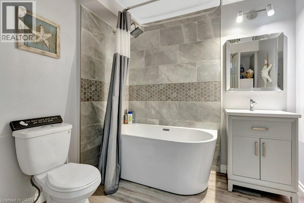 Freestanding soaking tub with a tiled shower surround featuring large format grey tiles and a hexagonal mosaic accent - 49 Small Court, Cambridge, ON - Indoor Photo Showing Bathroom