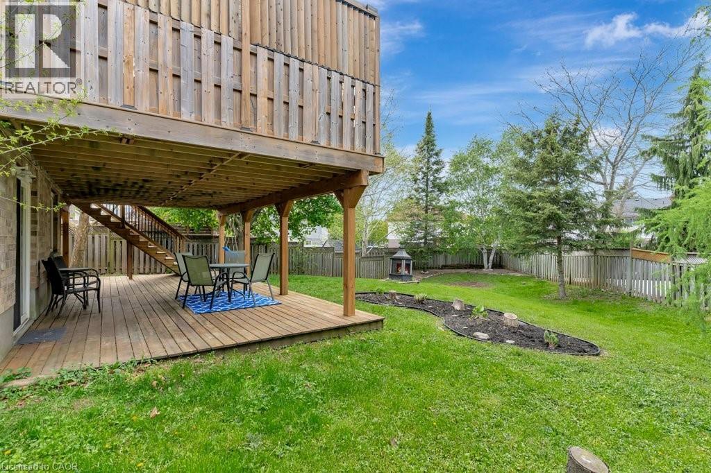 Expansive backyard featuring a large wooden deck with overhead protection, a curved garden bed, mature trees, and a wooden privacy fence - 49 Small Court, Cambridge, ON - Outdoor With Deck Patio Veranda