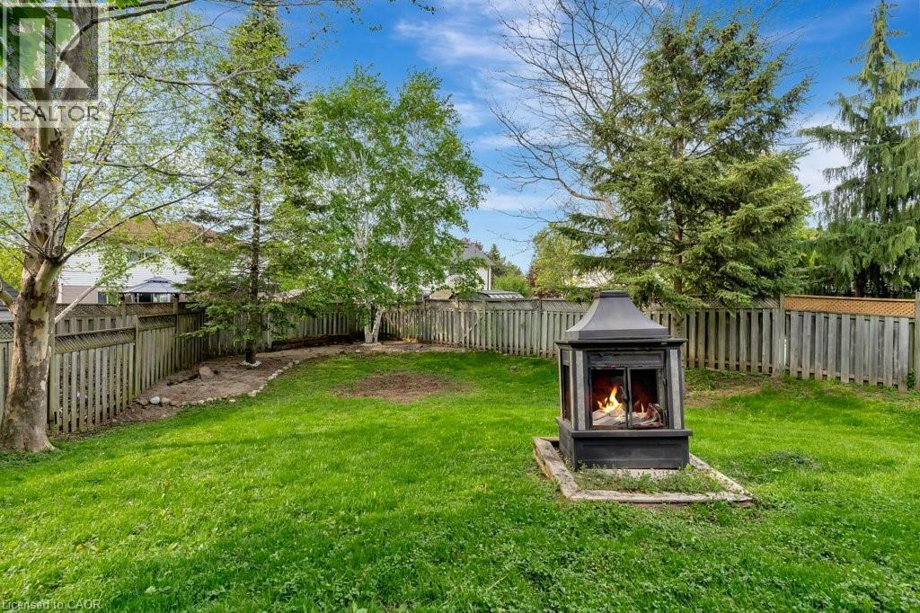 Expansive grassy yard featuring a black outdoor fireplace, surrounded by a wooden privacy fence - 49 Small Court, Cambridge, ON - Outdoor With Backyard