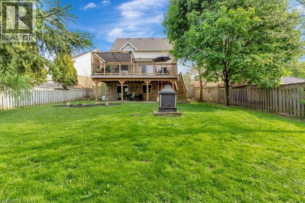 Expansive backyard featuring a large green lawn, a multi-level wooden deck with glass panel railings, and a stone-clad lower patio - 49 Small Court, Cambridge, ON - Outdoor With Deck Patio Veranda
