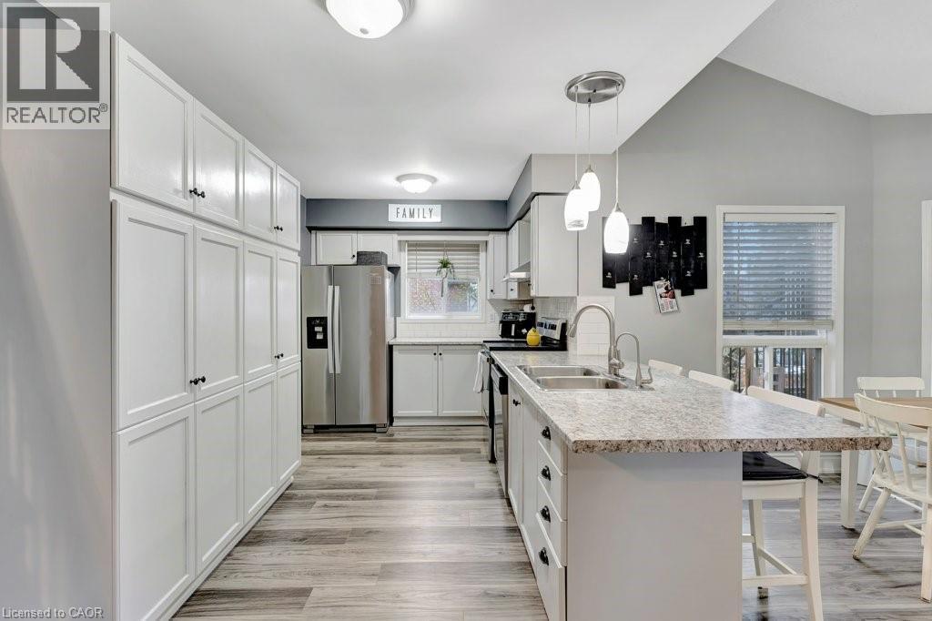 Spacious kitchen featuring extensive white cabinetry, stainless steel appliances, a large island with a stone-finish countertop, and wood-finish flooring - 49 Small Court, Cambridge, ON - Indoor Photo Showing Kitchen With Double Sink With Upgraded Kitchen