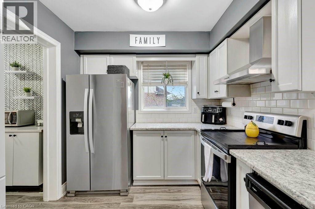Kitchen featuring white cabinetry, light granite-style countertops, subway tile backsplash, stainless steel appliances, and wood-finish flooring - 49 Small Court, Cambridge, ON - Indoor Photo Showing Kitchen